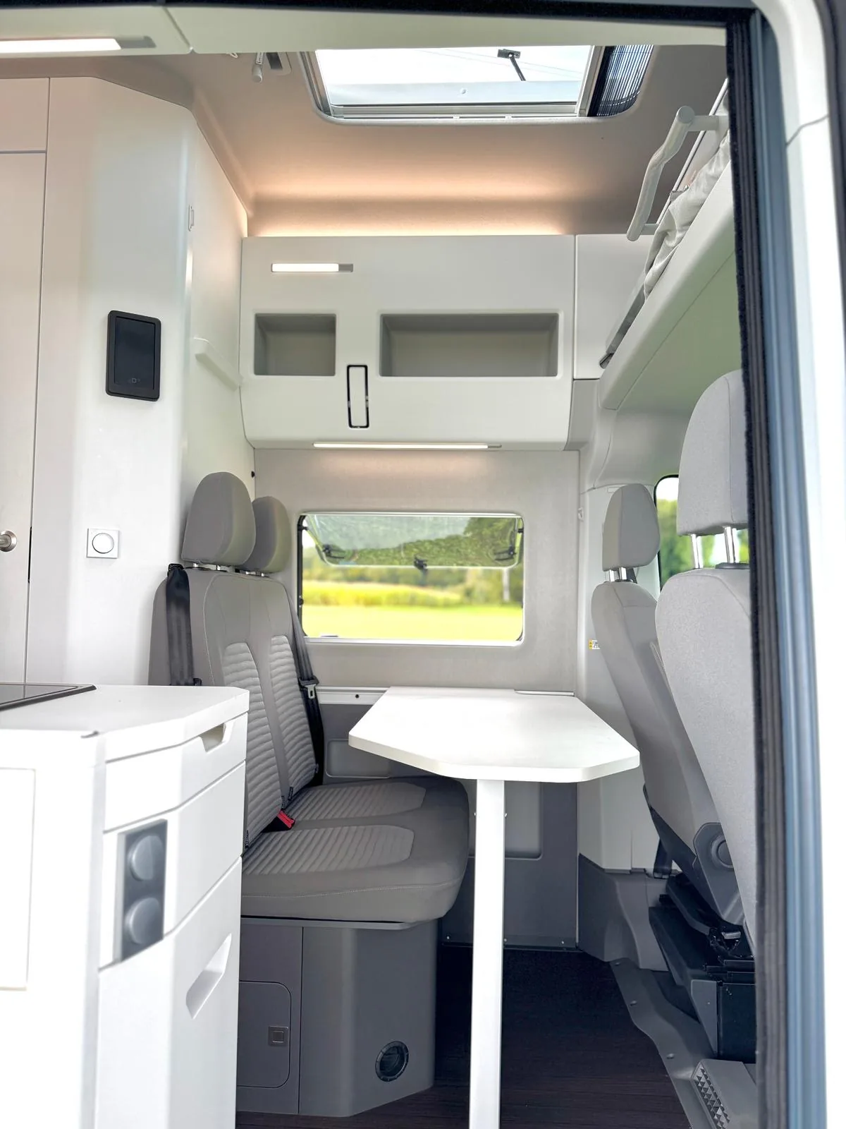 Sitzbankbereich des VW Grand California mit Tisch und Blick durch geöffnete Schiebetür