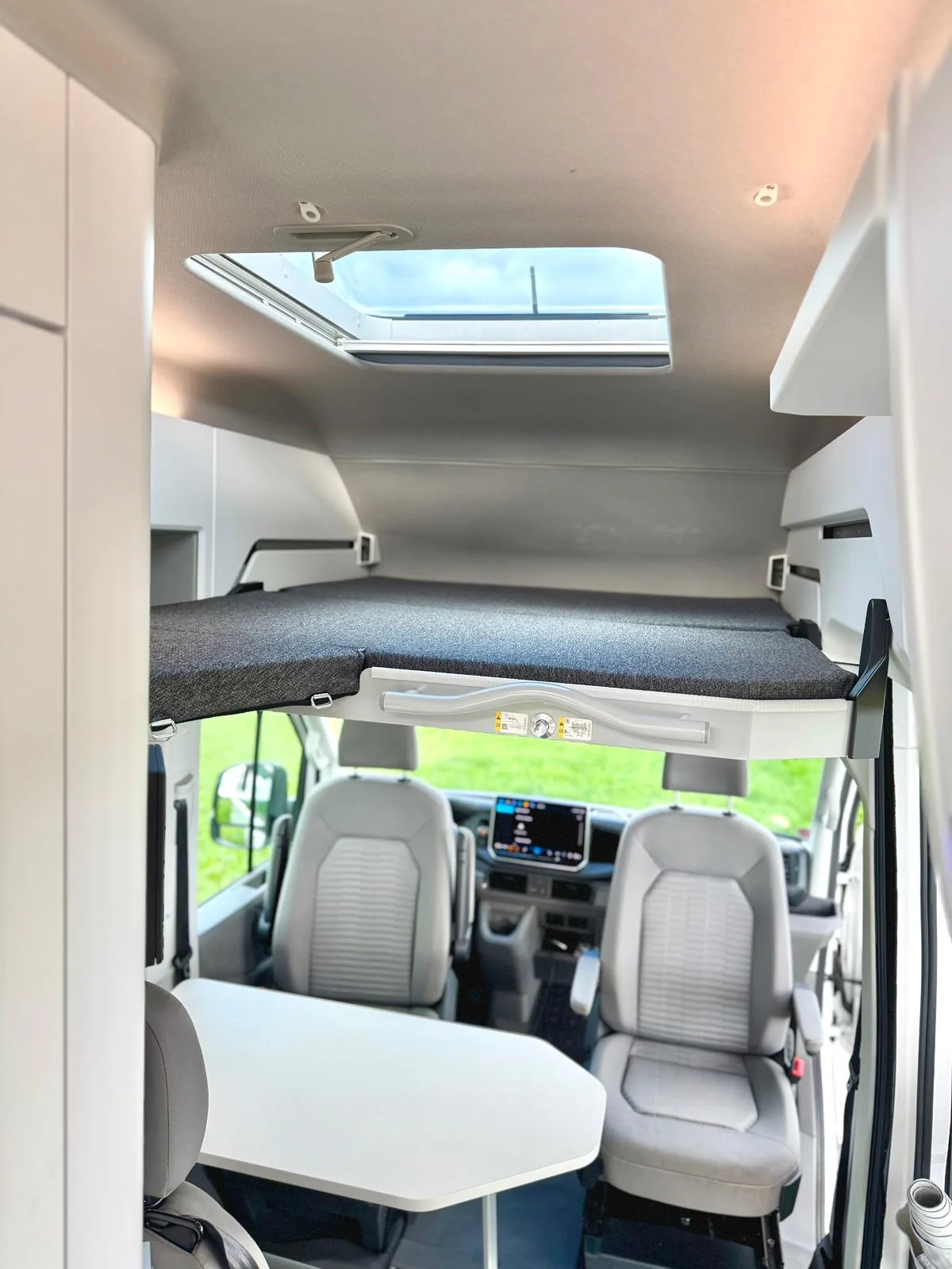 Ausgefahrenes Hängebett über den Fahrersitzen mit Blick durch Panoramascheibe auf grüne Landschaft