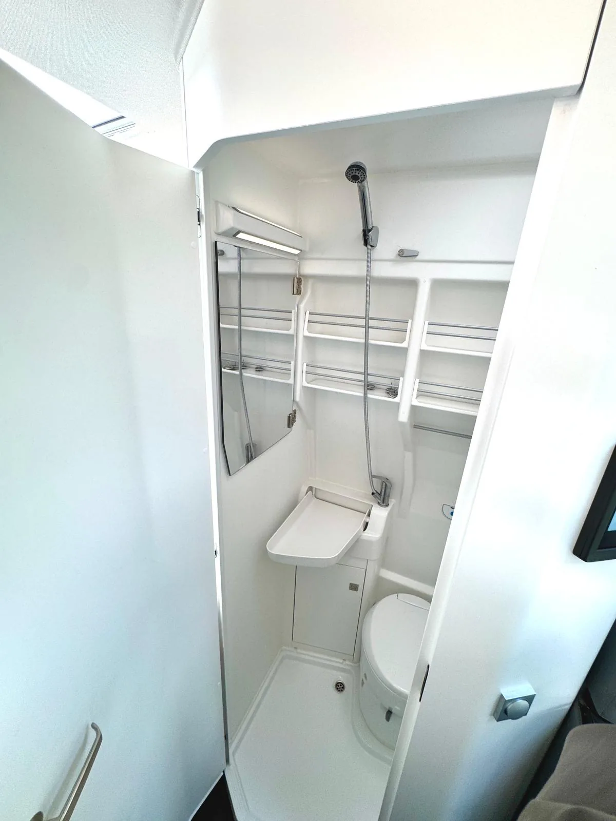 Detailansicht der Dusche mit Brausekopf, Ablageregalen und WC im Premium Camper